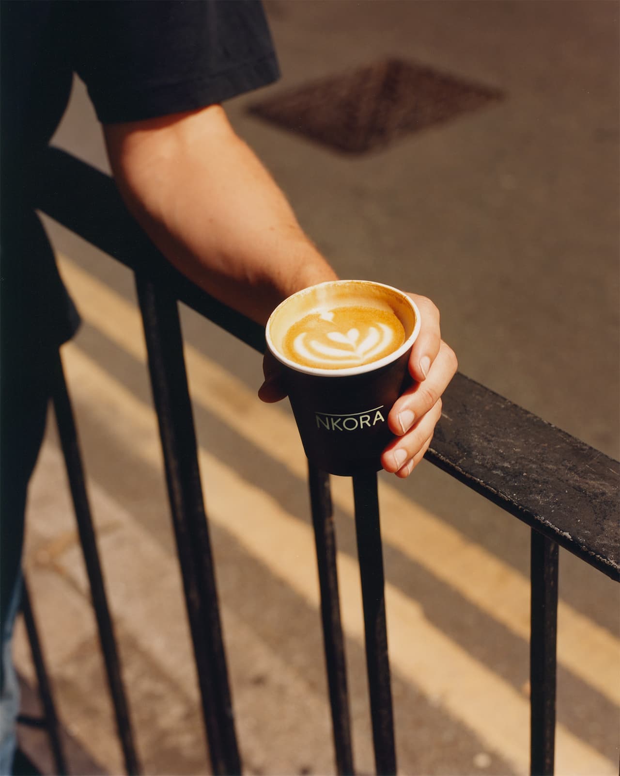 A person holding a NKORA coffee cup outdoor